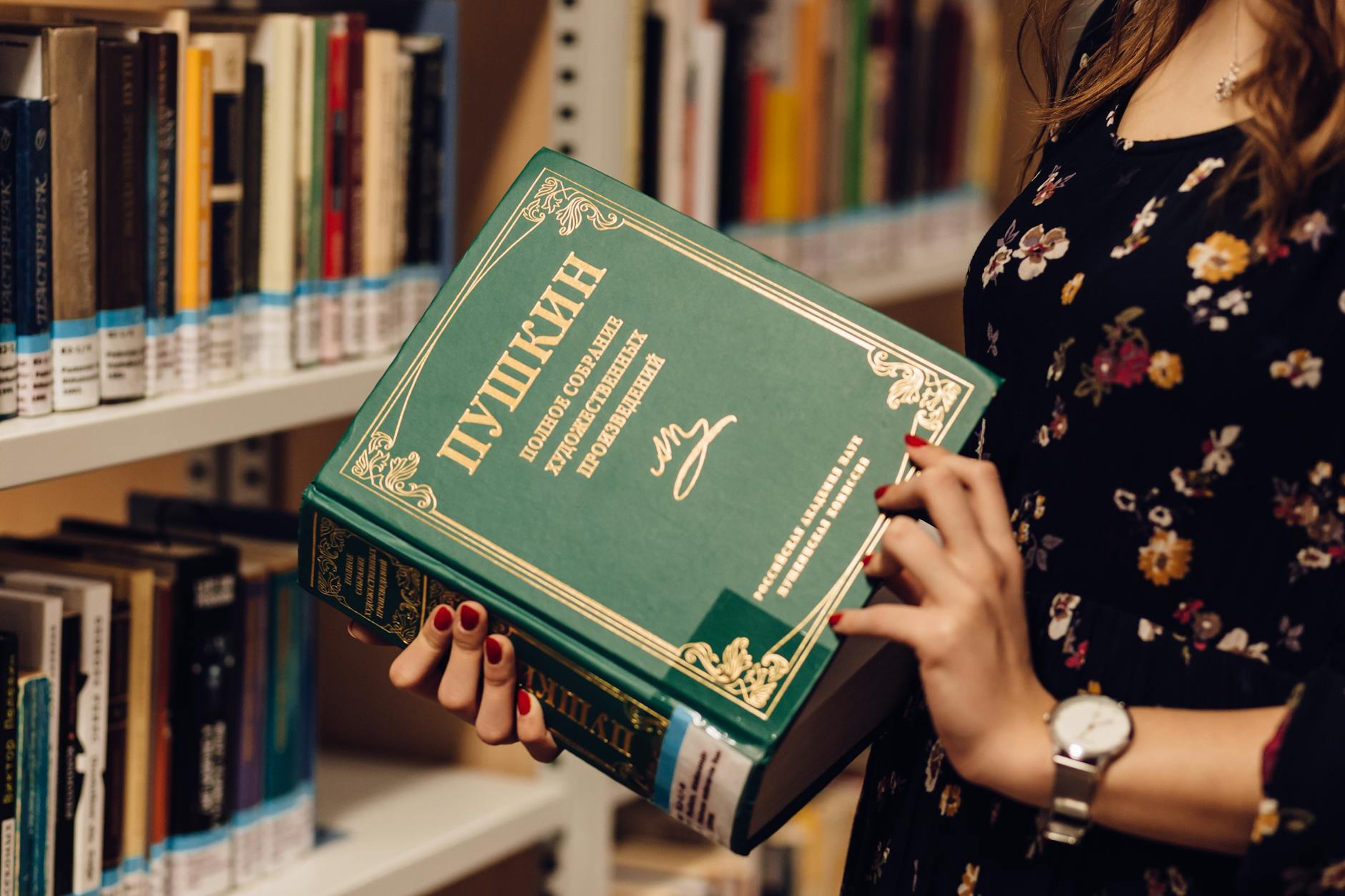 Kobieta w bibliotece w sukience z nadrukiem trzyma książkę z literaturą rosyjską