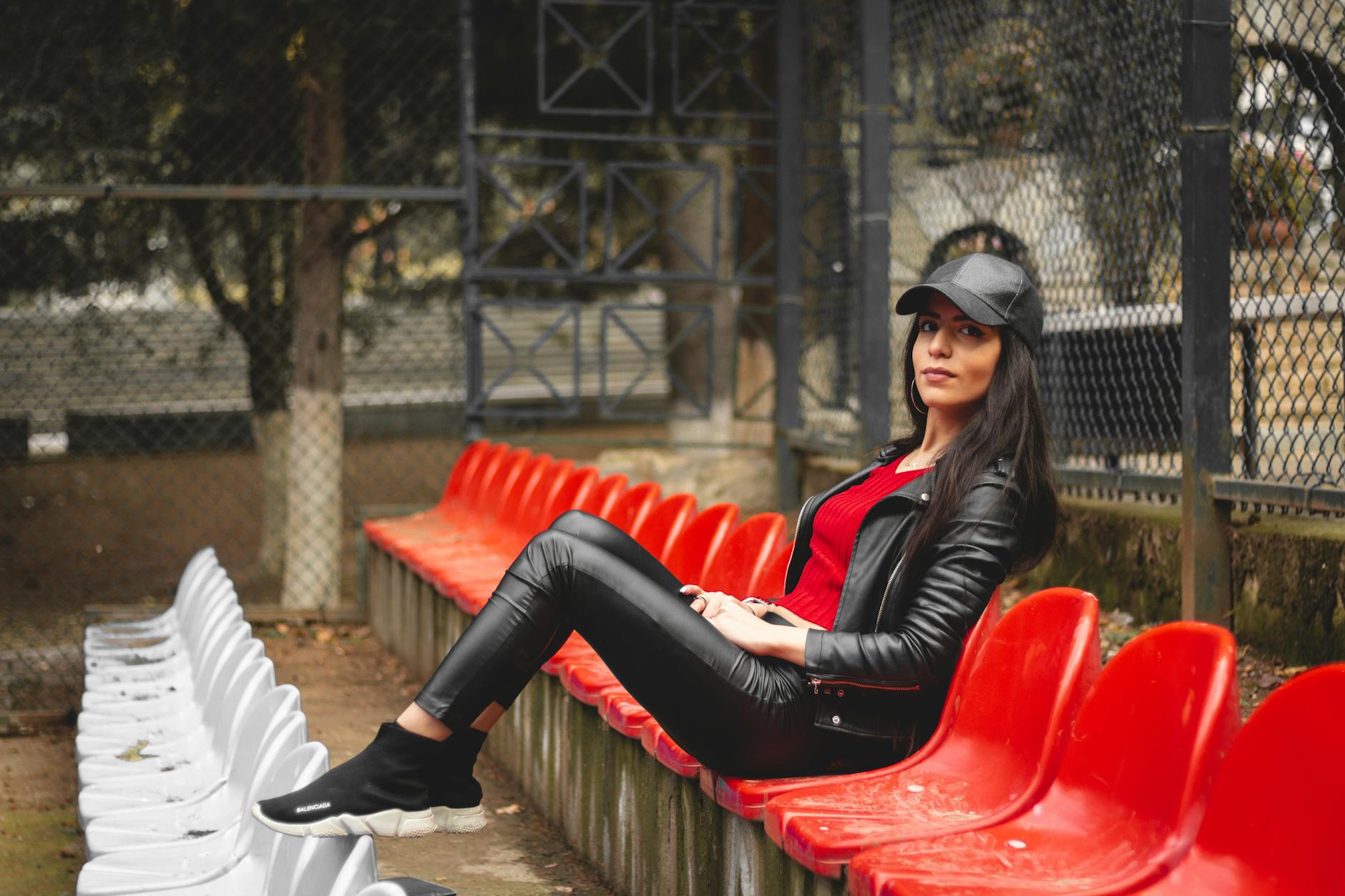 Stylowa kobieta w czarnej skórzanej stylizacji siedząca na czerwonych trybunach