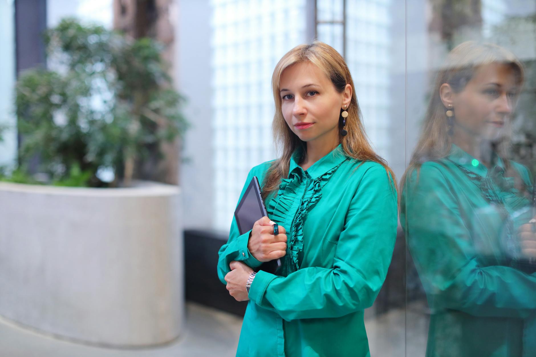 Elegancka kobieta w turkusowym topie biurowym oparta o szklaną ścianę