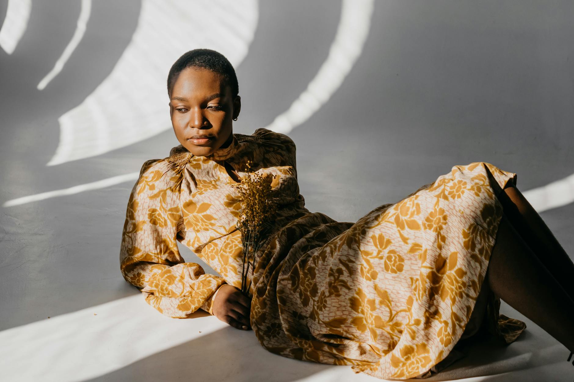 Kobieta w żółtej sukience w kwiaty pozuje w artystycznym świetle