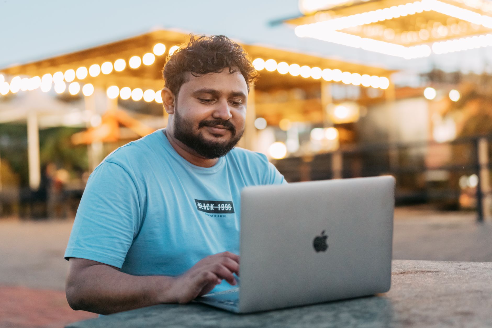 Mężczyzna uśmiecha się do laptopa, siedząc na zewnątrz przy światłach