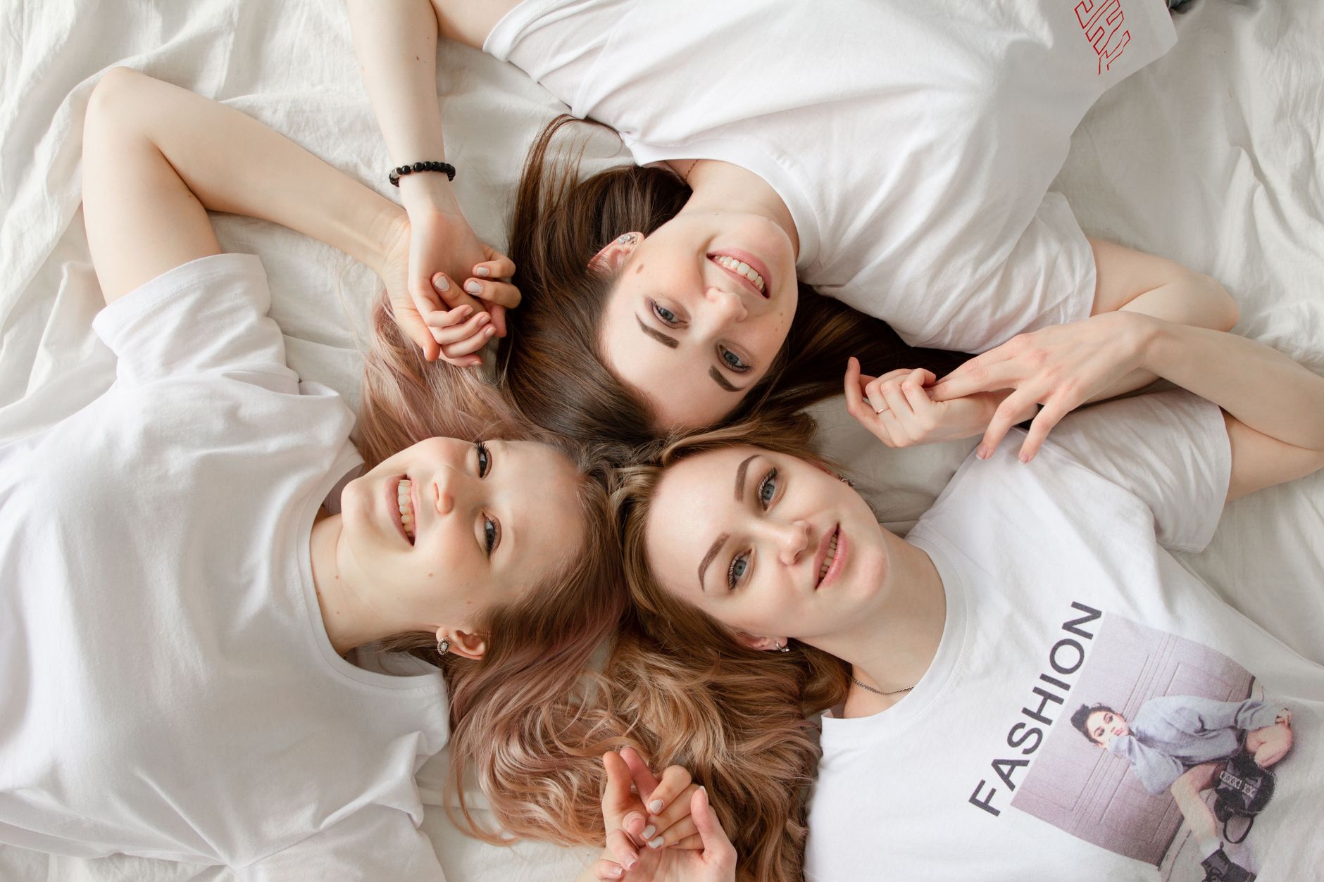 Trzy uśmiechnięte młode kobiety leżą na łóżku w casualowych stylizacjach